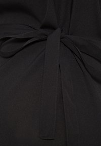 Tissu noir noué en un simple nœud avec deux extrémités libres, montrant une couture fine et une texture lisse.