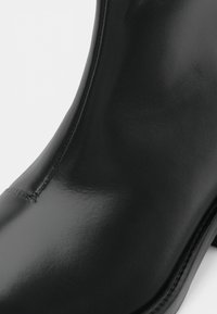 Melnas ādas potītes zābaki ar spīdīgu apdari, gludu tekstūru, sānu šuvēm un noapaļotu degunu. Iekļauts smalks papēdis.