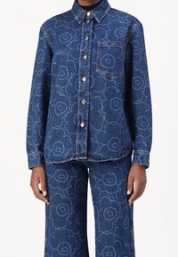 Zestaw koszuli i spodni dżinsowych, z kwiatowym wzorem w jasnoniebieskim kolorze na ciemnoniebieskim tle. Guziki z przodu i pojedyncza kieszeń na piersi.