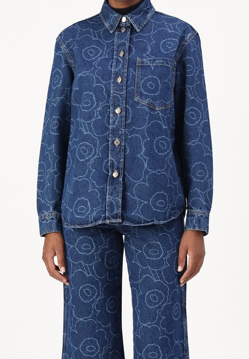 Zestaw koszuli i spodni dżinsowych, z kwiatowym wzorem w jasnoniebieskim kolorze na ciemnoniebieskim tle. Guziki z przodu i pojedyncza kieszeń na piersi.