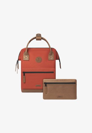 Sac à dos en tissu rouge avec des accents et une poignée en brun texturé, comportant une poche zippée à l'avant et une trousse assortie en brun à côté.