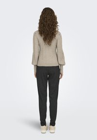 Pull en tricot beige avec un motif texturé, manches ballons, associé à un pantalon slim gris foncé et des baskets couleur crème.