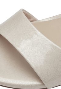 Gros plan sur une sandale beige avec une large sangle texturée traversant la semelle.