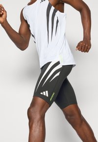 White athletic tank top with black stripes and green "ADIZERO" logo, paired with black fitted shorts featuring white angular designs and branding.