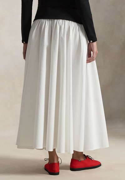 Jupe longue plissée blanche avec taille élastique, associée à des chaussures rouges à lacets. La jupe présente une finition lisse et texturée.