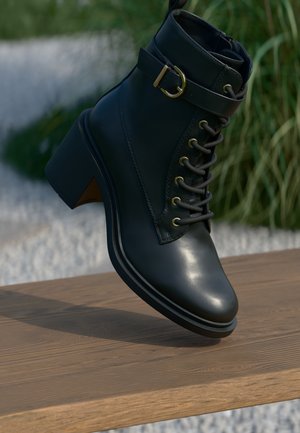 Crne kožne anklet čizme s sjajnim finišem, vezanje sprijeda, zlatni detalji i blok peta. Sadrži detalj s remenom i kopčom.