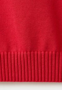 Gros plan sur la partie inférieure d'un pull rouge en tricot montrant un ourlet côtelé détaillé et une texture tricotée.