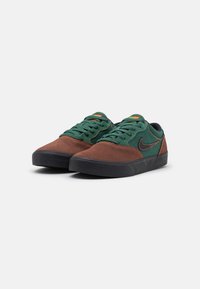 Brown and green suede sneakers with black rubber sole, featuring green laces and orange accents, streamlined design, and padded collar.