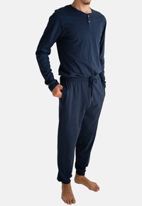 Maglietta a maniche lunghe blu navy con scollatura henley e due bottoni, abbinata a pantaloni jogger coordinati con vita elasticizzata e tasche.