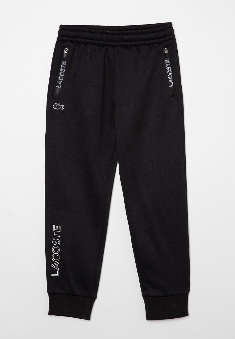 Pantalons de survêtement Lacoste noirs avec taille élastique, poches latérales zippées, texte Lacoste blanc sur les poches et la jambe gauche, et logo crocodile près de la poche.