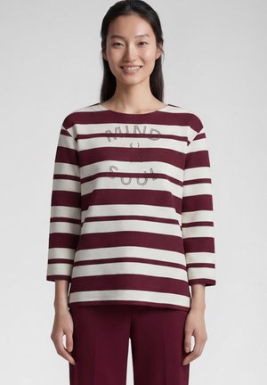 Woman wearing a long-sleeve maroon and white striped shirt with "Mind & Soul" text and maroon pants, standing against a plain background.