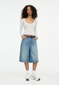 Maglietta bianca a maniche lunghe, culotte in denim azzurro chiaro con vestibilità dritta, cintura nera, calze bianche e scarpe da ginnastica argentate.