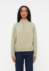 Suéter de cuello con cremallera en verde claro, confeccionado en material de punto suave, con ribetes en el dobladillo y las muñecas, y un diseño minimalista con un tirador de cremallera redondo.