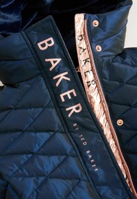 Gesteppten navy Puffermantel mit hohem Kragen, versehen mit roségoldenen Akzenten und einem auffälligen "BAKER"-Logo an der Seite des Reißverschlusses.