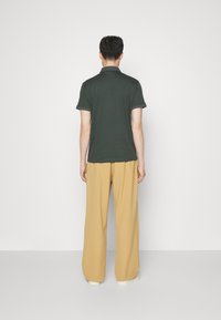 Polo shirt vert foncé à manches courtes, associé à un pantalon beige clair ample. Texture de tissu lisse avec une coupe décontractée.