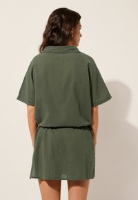 Vestido corto verde con un corte relajado, mangas cortas y cuello de camisa. Presenta una cintura elástica y una tela suave y ligera.