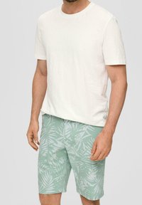 T-shirt bianca a maniche corte abbinata a pantaloni corti verde menta con un motivo foglioso bianco. Il tessuto appare leggero e informale.