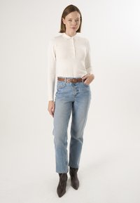 Kremfarvet langærmet poloshirt med knaplukning, kombineret med lyseblå højttaljede jeans og brunt bælte, suppleret med mørkebrune ankelstøvler.