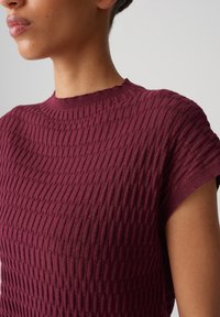 Burgundy textured knit top featuring a round neckline and short sleeves with a ribbed pattern, made from a soft fabric.