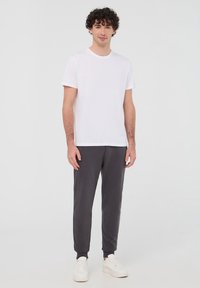 Biała bawełniana koszulka i ciemnoszare spodnie dresowe, obie o luźnym kroju. Dresy mają elastyczne mankiety i są połączone z białymi trampkami.