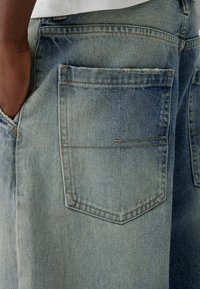 Ljusblå denim jeans med en urtvättad finish, som har två bakfickor och synliga sömnadsdetaljer. Texturen är mjuk och sliten.