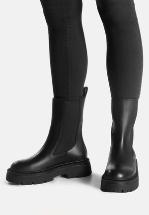 Schwarze Leder-Stiefeletten mit einer klobigen Gummisohle, elastischen Seitenteilen und einer Schlaufe zum einfachen An- und Ausziehen. Glatte Textur und elegantes Design.