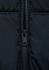 Black puffer jacket segment z zadrgo na sredini z črnimi zobmi in trakcem za poteg, obdan z quilted teksturo in gladkim materialom.