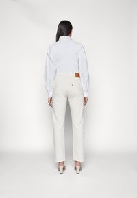 Pantalones blancos de talle alto y una blusa ligera azul celeste con mangas abullonadas. Marca Levi's visible en el bolsillo trasero.