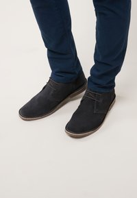 Dunkelblaue Wildlederschuhe mit flacher Sohle, Schnürdetails und minimalistischem Design. Kombiniert mit navyfarbenen Hosen.