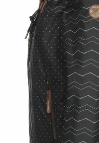 Schwarze Jacke mit Punkt- und Zickzackmustern, mit einer Reißverschlusstasche und verstellbarem Kordelzug. Akzentuiert durch ein braunes Logoetikett.