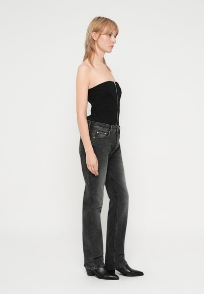 Čierny bezramenný top s predným zipsom, v kombinácii so sivými rovnými džínsami. Čierne členkové topánky dotvárajú outfit. Minimalistický dizajn, bezšvový vzhľad.