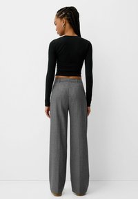 Haut à manches longues noir associé à un pantalon large à rayures grises. Présente un design ajusté et une texture lisse. Vue de dos montrée.