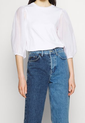 Haut blanc à manches bouffantes et transparentes, associé à un jean en denim bleu moyen taille haute avec une coupe classique et un léger délavé.