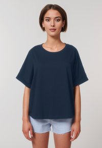 T-shirt oversize blu navy con scollo rotondo e maniche corte, realizzata in tessuto morbido; abbinata a pantaloncini di denim azzurro con bordi sfilacciati.