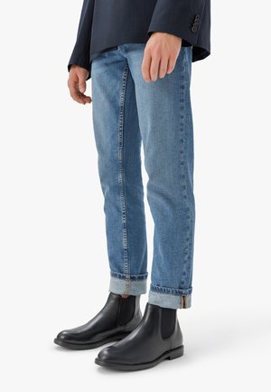 Stivali Chelsea in pelle nera abbinati a jeans di denim azzurro chiaro, leggermente risvoltati sui polsini, che mostrano una texture liscia e una vestibilità su misura.