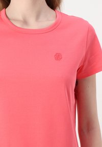 Kortermet t-skjorte med rund hals i klar korallfarge, med en subtil brodert logo på brystet og en glatt, lett tekstur.