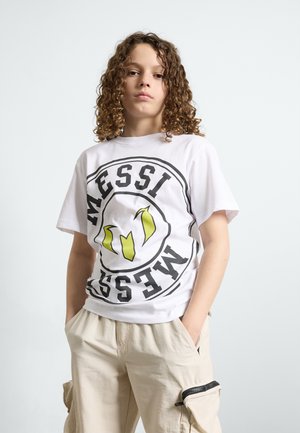 White t-shirt with black and neon yellow "MESSI" graphic, paired with beige cargo pants featuring zippered pockets and loose fit.