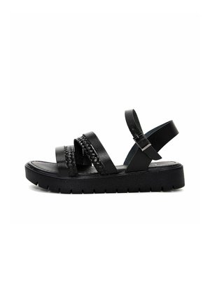Black sandals with a flat sole, featuring three wide straps and one braided strap. Adjustable ankle strap with a buckle detail.