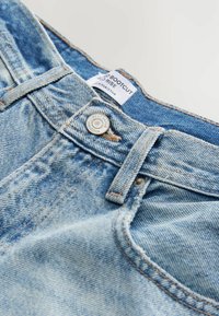 Lichtblauwe denim bootcut jeans met een vervaagde textuur, met een metalen knoopsluiting en een label dat maat en herkomst aangeeft.