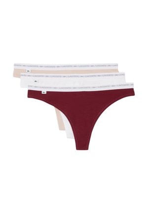 Tres tangas de mujer en beige, blanco y rojo oscuro, cada una con una cintura blanca que lleva el logo de Lacoste y el emblema del cocodrilo.