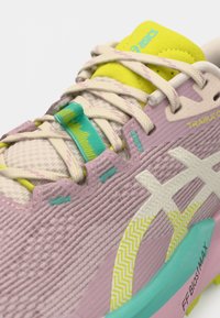 Ténis de corrida Asics com parte superior texturizada rosa, logótipo branco, detalhes amarelos na língua e sola turquesa com padrão em ziguezague.