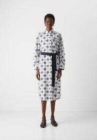 Abito a maniche lunghe con bottoni, in tessuto a motivo geometrico blu navy e bianco, con vita cinchata e cintura abbinata, e lunghezza fino al ginocchio.