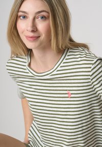 Maglietta a righe verde e bianca, colletto girocollo, maniche corte, con un piccolo logo ricamato rosa sul petto. Tessuto soffice.