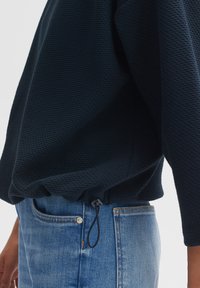 Felpa texturizzata di colore blu navy con coulisse in vita, abbinata a jeans in denim azzurro chiaro con chiusura a bottone e tasche laterali.