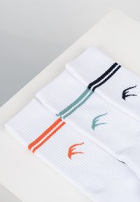 Calcetines blancos acanalados con tres rayas de colores: negro, azul verdoso y naranja, con acentos de logotipo de pájaro en colores a juego.