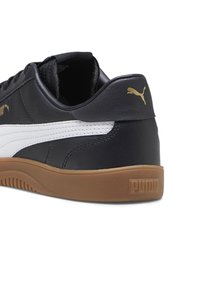 Czarne skórzane sneakersy Puma z białym paskiem, gumową podeszwą oraz złotym logo Puma na pięcie i boku.