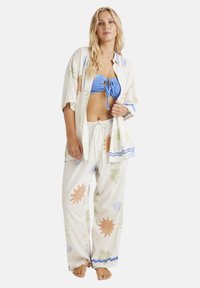 Floral-patterned pajama set featuring a light fabric; loose-fit pants with an elastic waistband, short-sleeve button-up shirt, and blue bikini top.