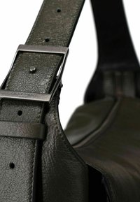 Olivgrüner Lederarmband mit strukturierter Oberfläche, ausgestattet mit einer Metall-Schnalle und Anpassungslöchern, befestigt an der Seite einer Tasche.