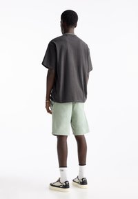 Chemise ample à manches courtes gris foncé, short vert menthe, baskets noires et crème, chaussettes blanches, design minimaliste et tissu texturé.