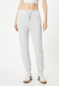 Lys grå sweatpants lavet af blødt stof, med en elastisk talje med snørre, sidelommer og ribkantede ankler.